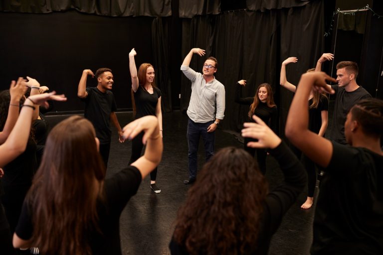 Teacher With Male And Female Drama Students At Performing Arts School In Studio Improvisation Class